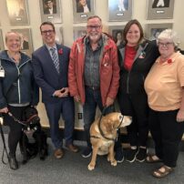 Jennifer Sanderson, Brad Trivers, Russell McCabe, Shannon Noonan and Karen McRae along with two service dogs pose for a photo after first session of debate of the Service Dog Act on Nov 7th 2024.