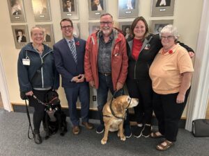 Jennifer Sanderson, Brad Trivers, Russell McCabe, Shannon Noonan and Karen McRae along with two service dogs pose for a photo after first session of debate of the Service Dog Act on Nov 7th 2024.